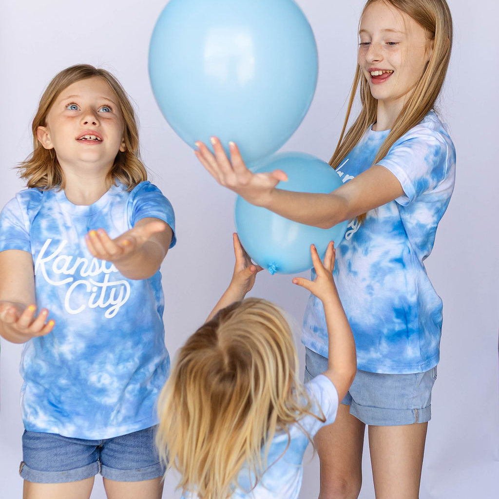 Three children in matching blue tie-dye outfits with balloons on a white background